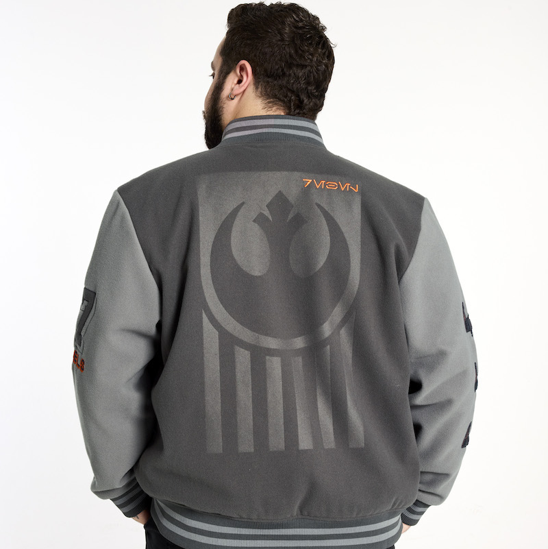 Bearded man facing away from camera wearing the Loungefly COLLECTIV Star Wars Rebel Alliance VRSITY Jacket and showing off the back of the jacket, which has the Rebel Alliance symbol on it and the word "Rebel" embroidered in Aurebesh.